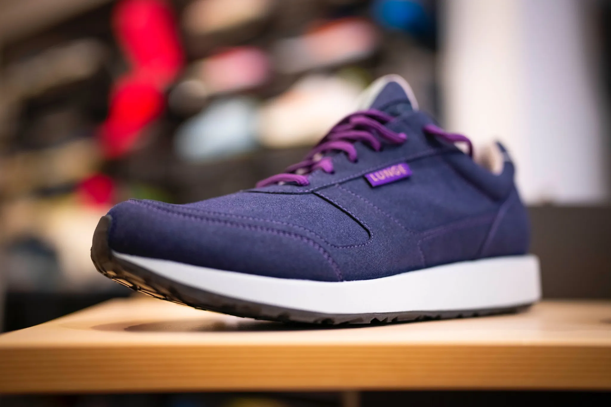 Ein marineblauer Turnschuh mit lila Schnürsenkeln und weißer Sohle ist auf einer Holzfläche mit unscharfem Hintergrund abgebildet.